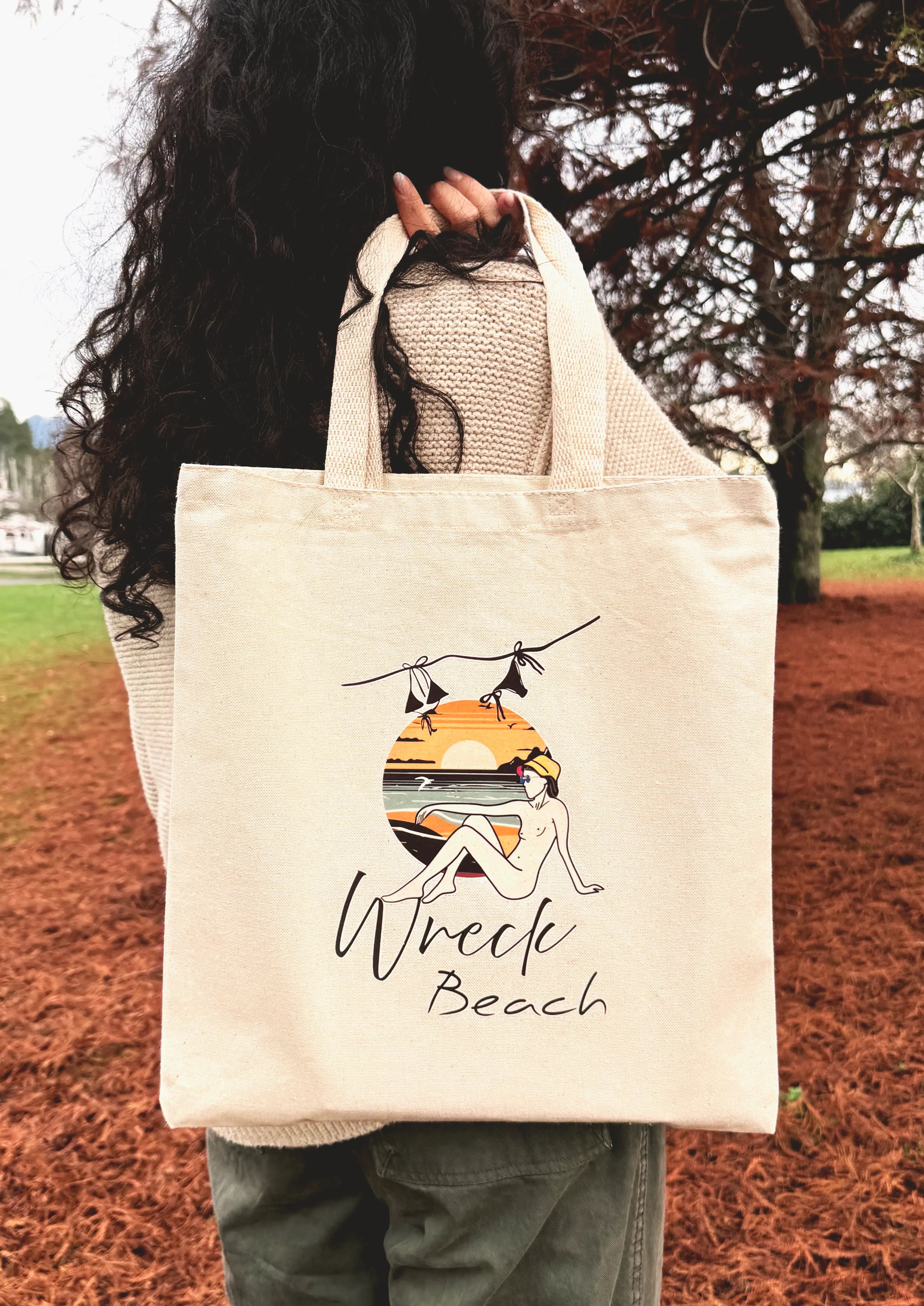 Canvas tote bag with Wreck Beach sunset illustration being carried over the shoulder in a park setting