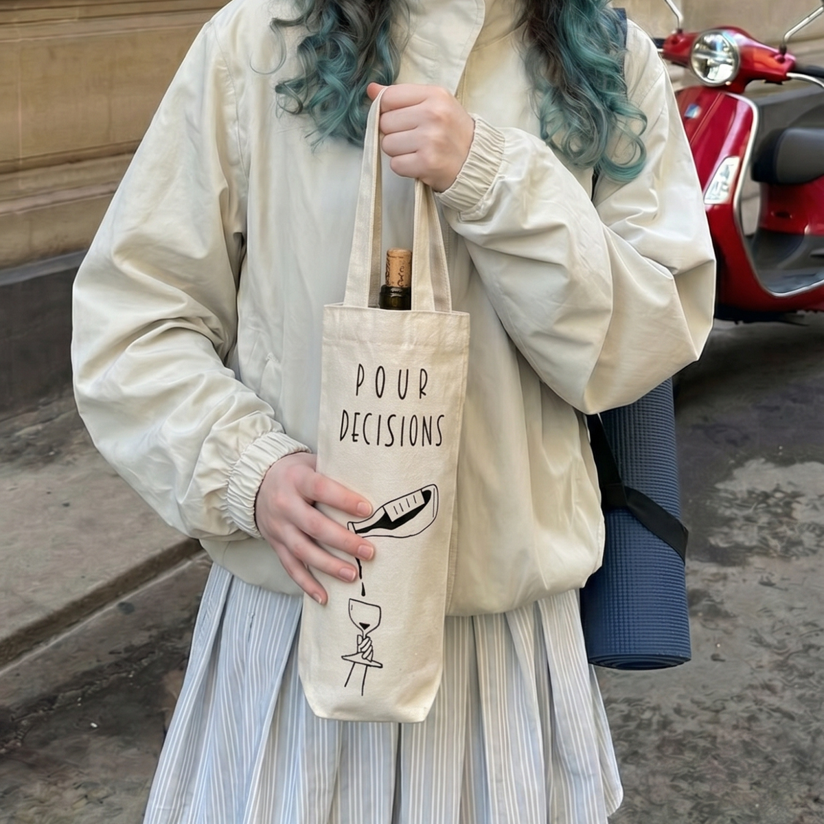 Person holding a tote bag with text and a bottle, standing next to a red scooter.