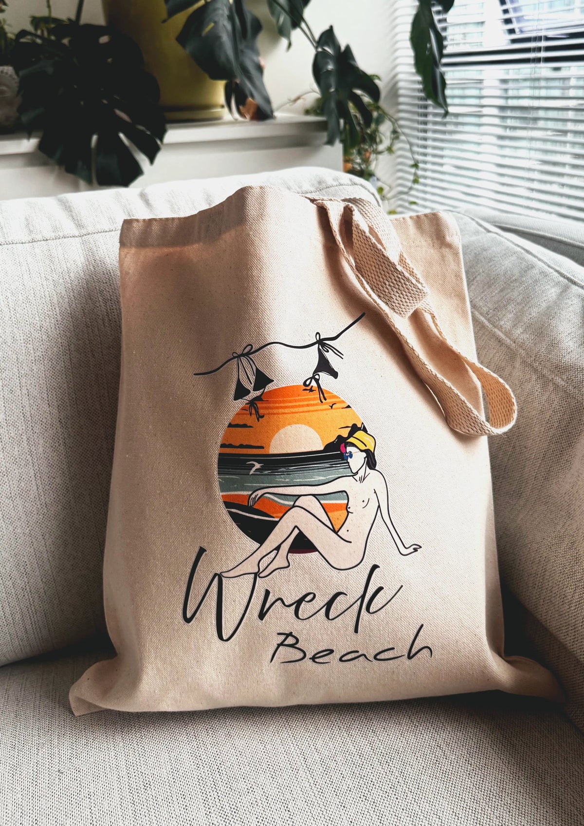 Wreck Beach canvas tote bag placed on a sofa in a cozy indoor setting with plants