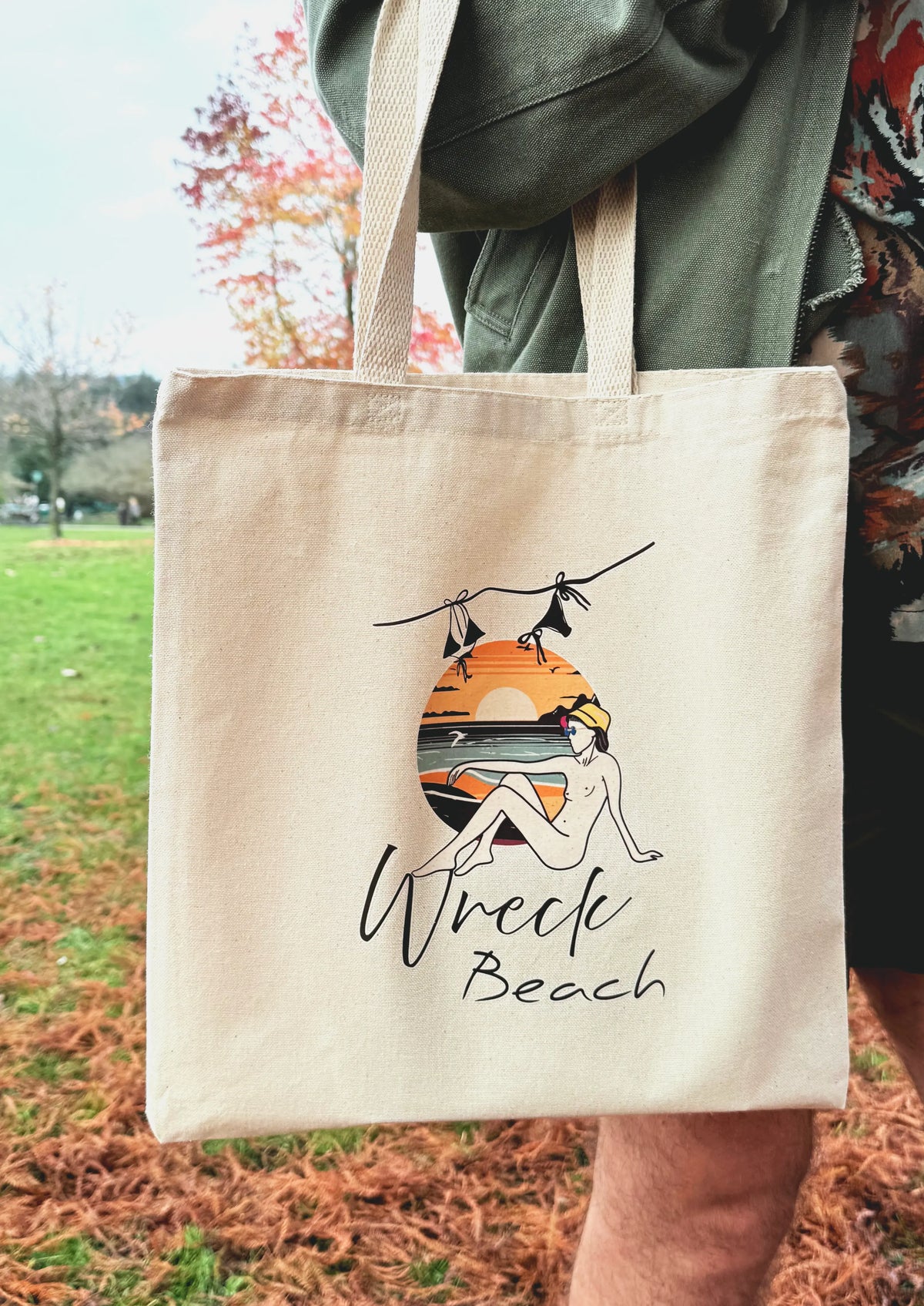 Natural canvas Wreck Beach tote bag held outdoors with printed sunset beach design