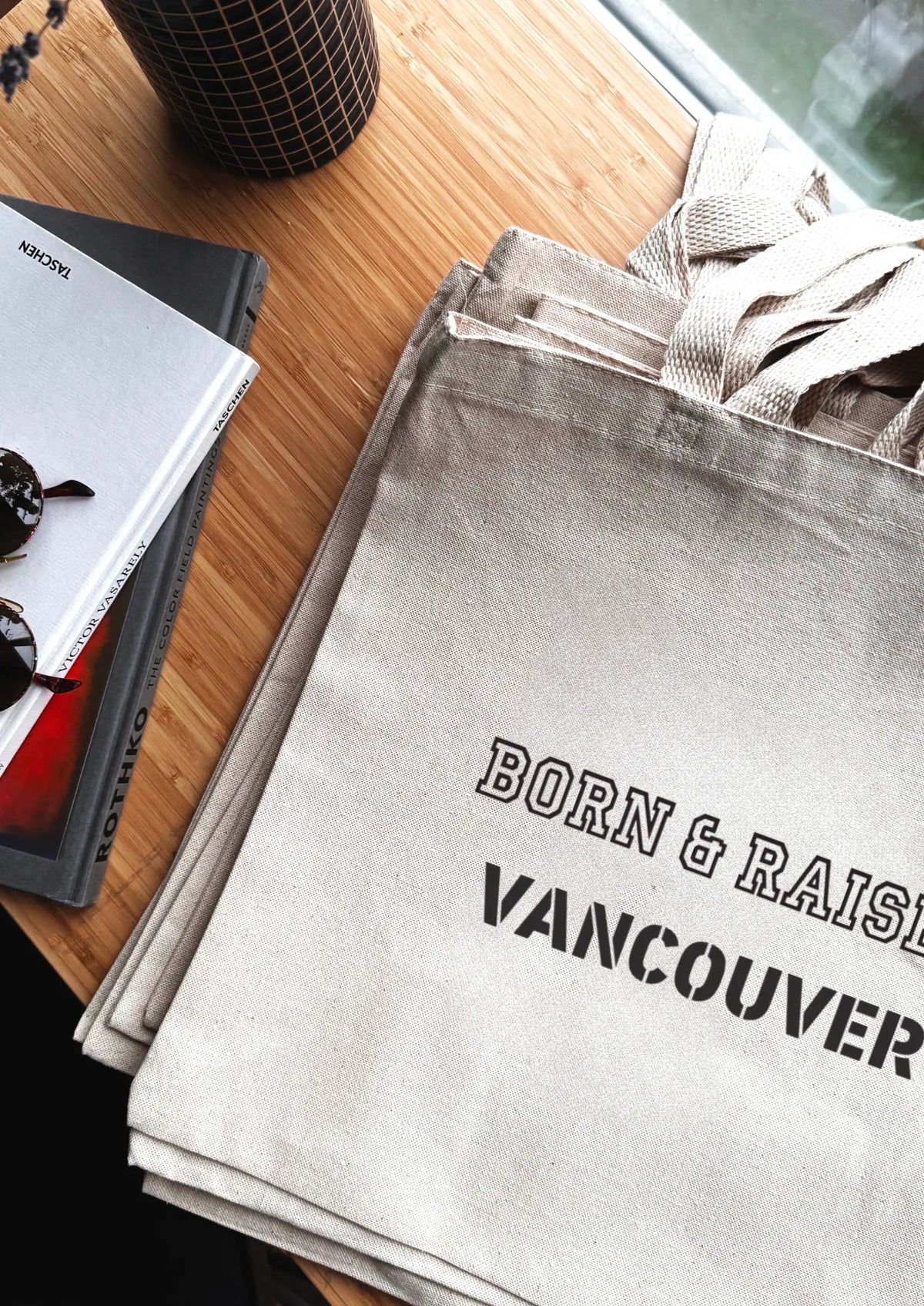Gray tote bag with 'Born & Raised Vancouver' text on a wooden surface.