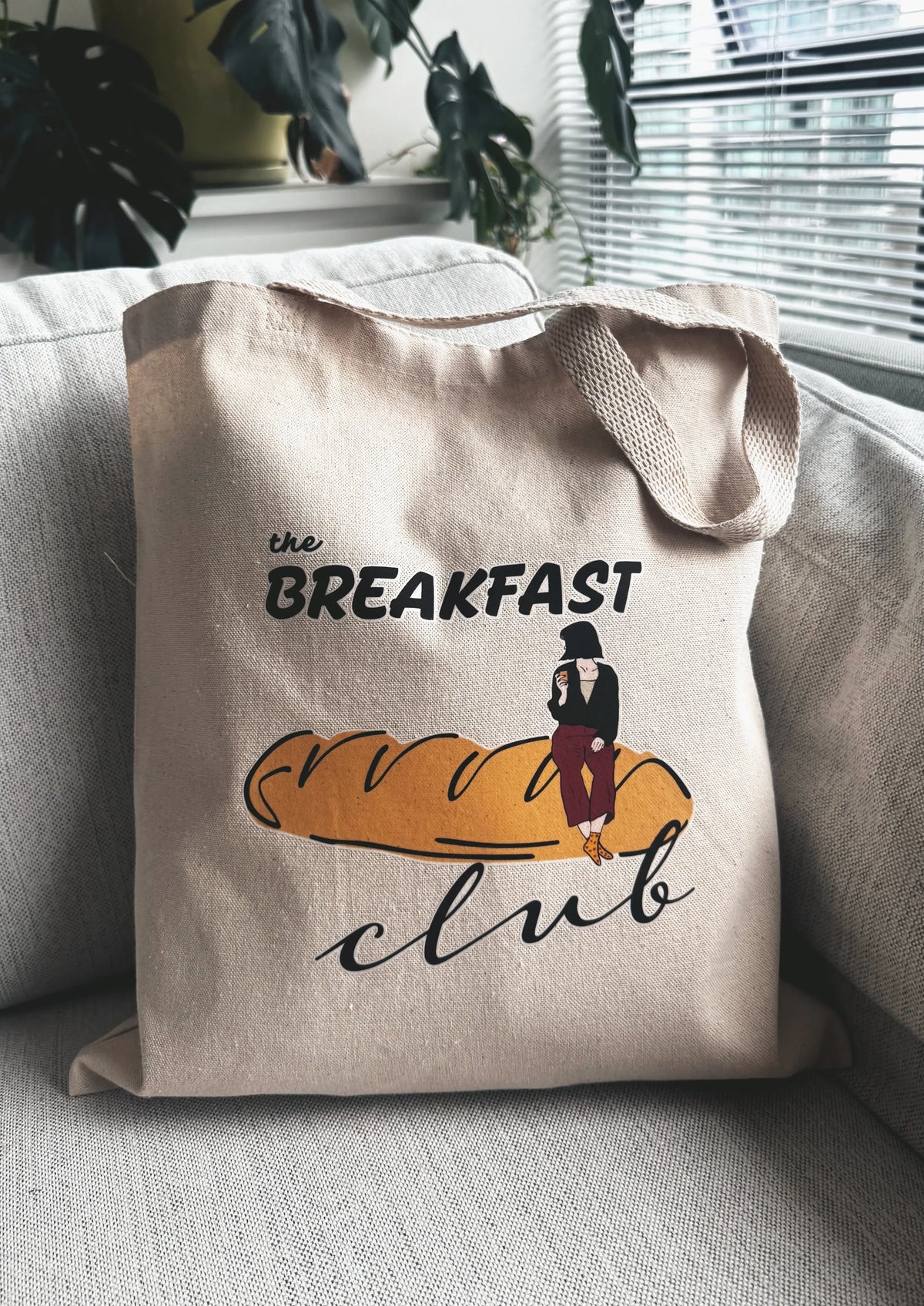 Breakfast Club line art canvas tote bag resting on a sofa in a bright living room