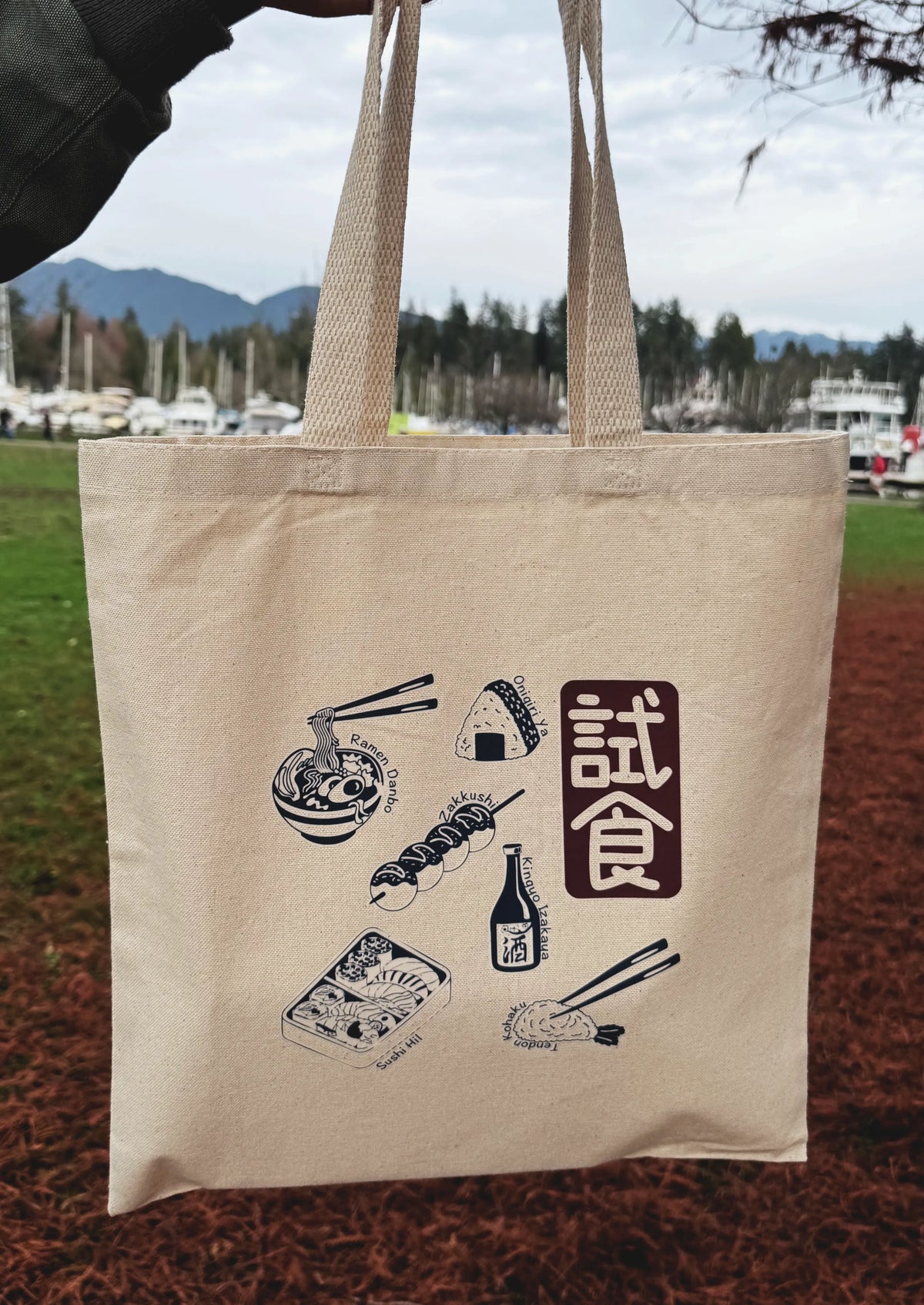 Beige tote bag with Japanese food illustrations and text in an outdoor setting