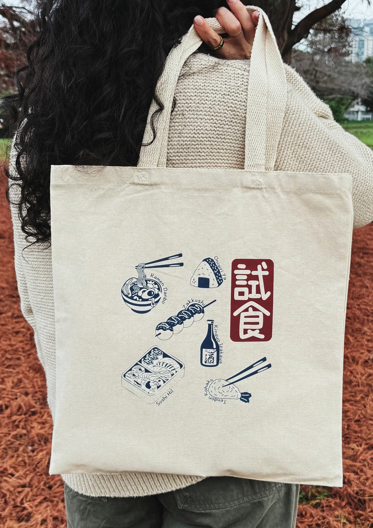 Person holding a tote bag with Japanese food illustrations and text.