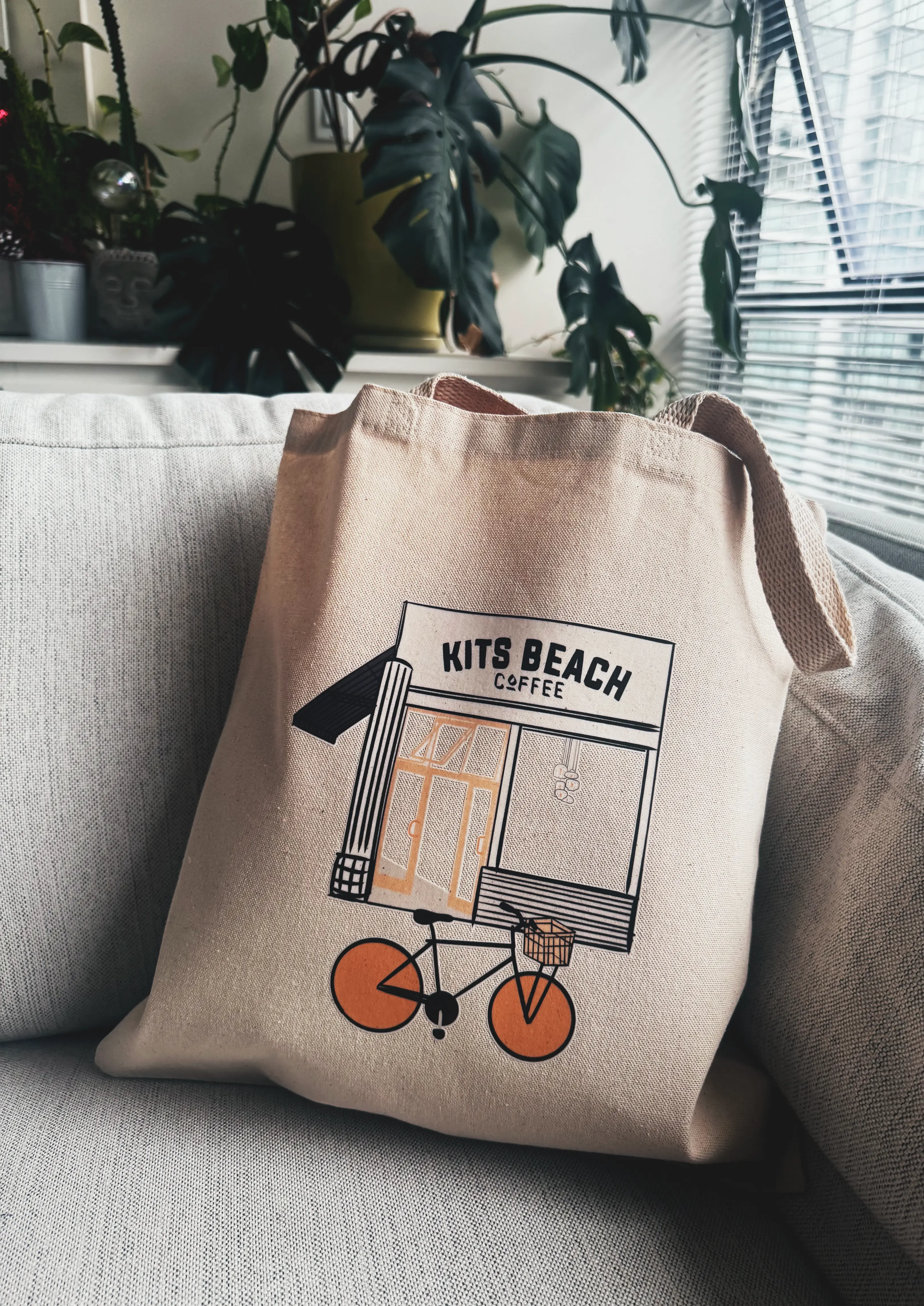 Beige tote bag with 'Kits Beach Coffee' design on a white couch