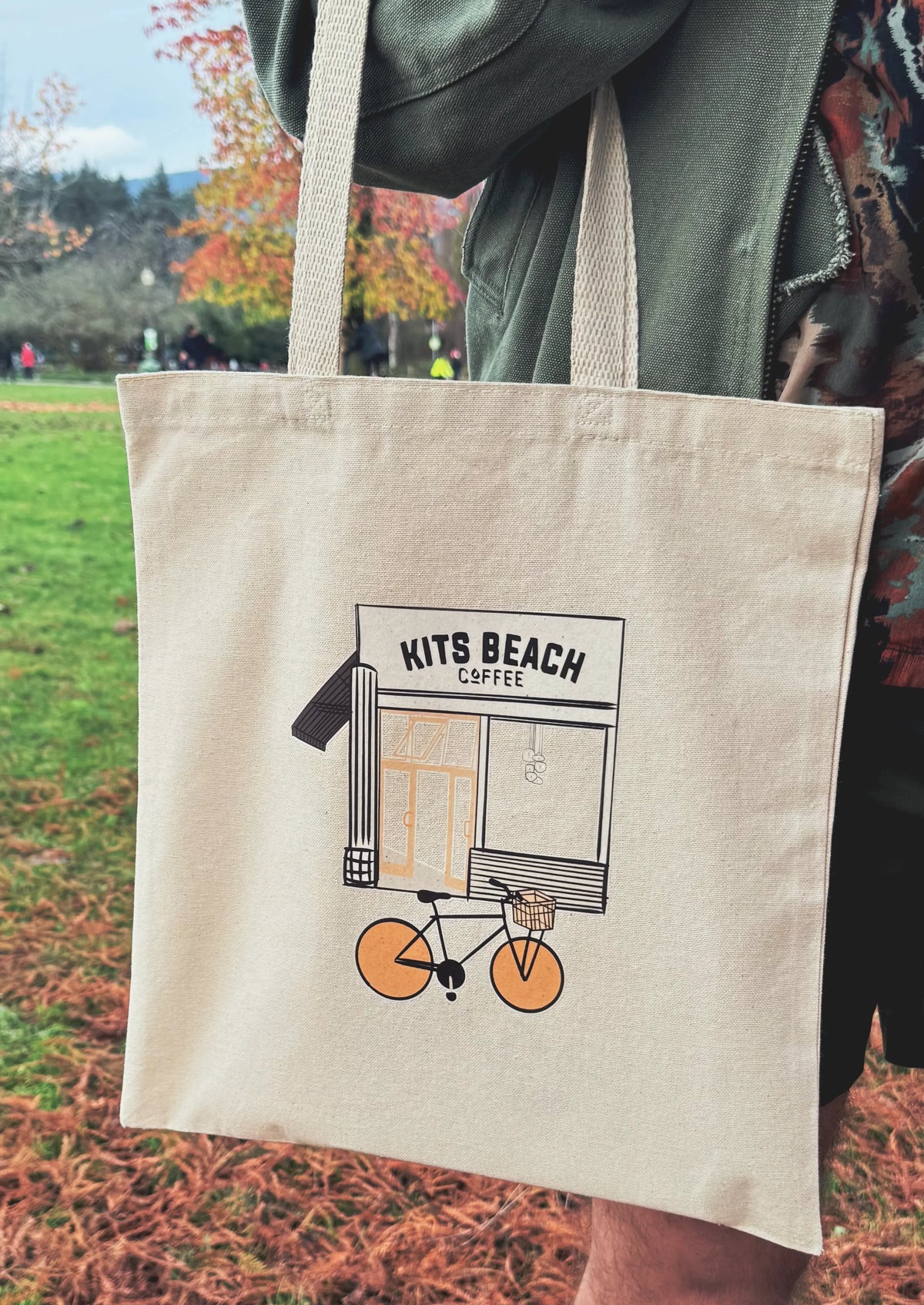 Tote bag with 'Kits Beach Coffee' design held by a person outdoors.