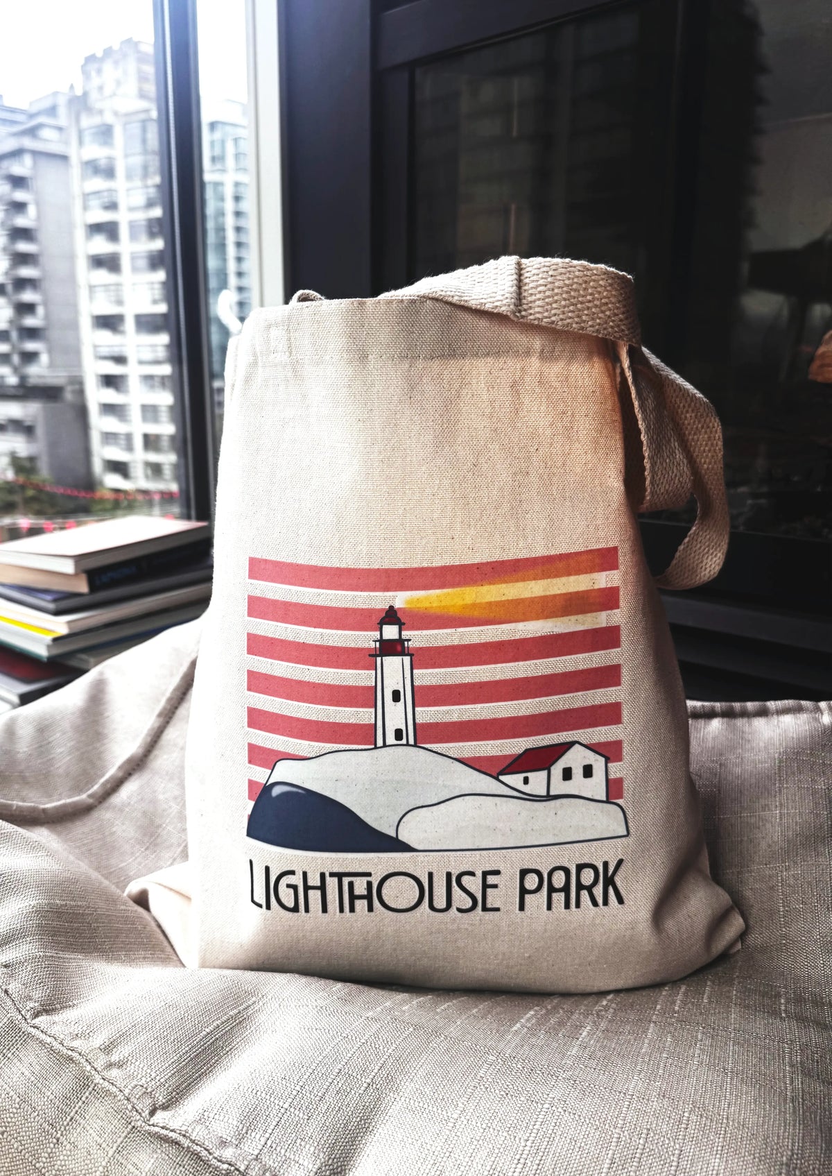 Beige tote bag with a lighthouse design and 'Lighthouse Park' text on a couch.