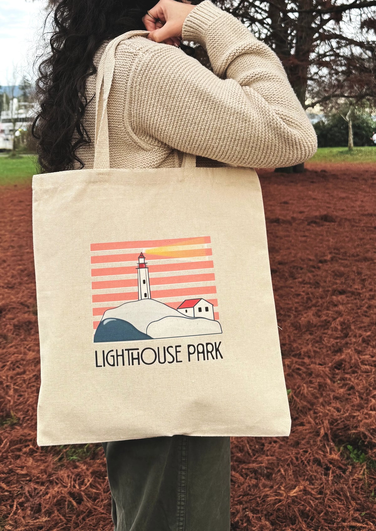 Person holding a tote bag with a lighthouse design and 'Lighthouse Park' text.