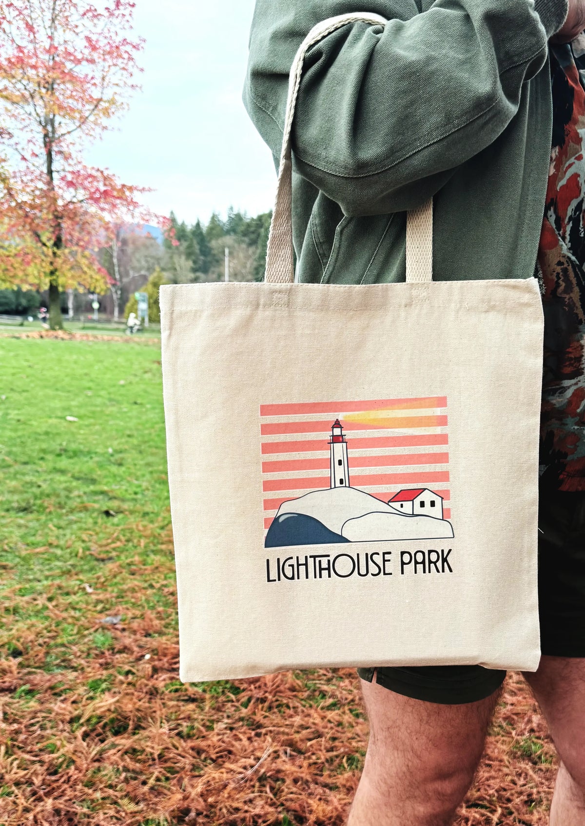 Tote bag with 'Lighthouse Park' design held by a person in an outdoor setting.