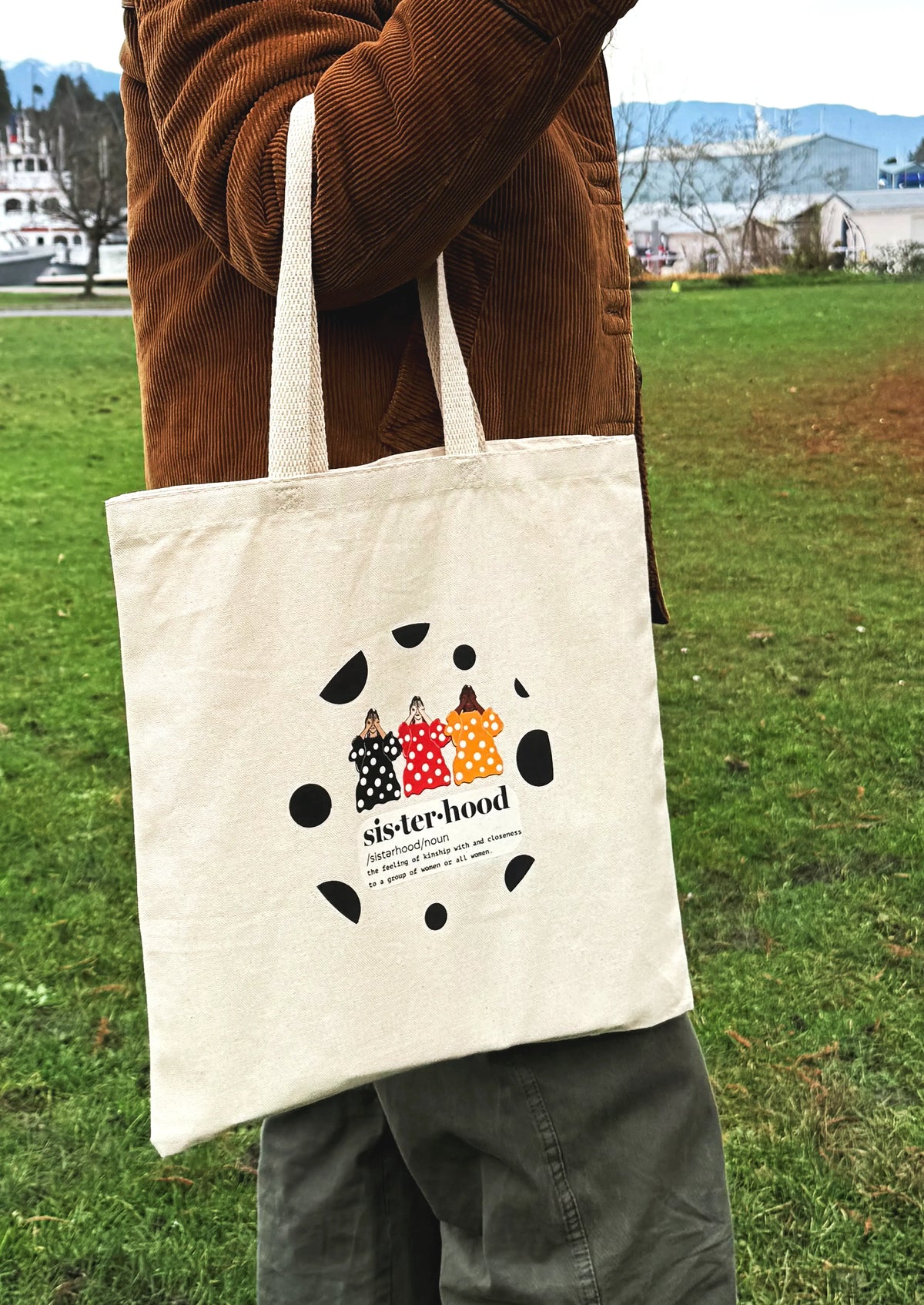 Front view of Sisterhood line art canvas tote bag hanging outdoors in a park