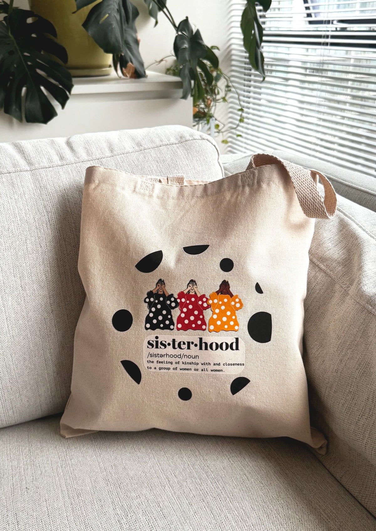 Sisterhood line art canvas tote bag resting on a sofa in a bright living room setting