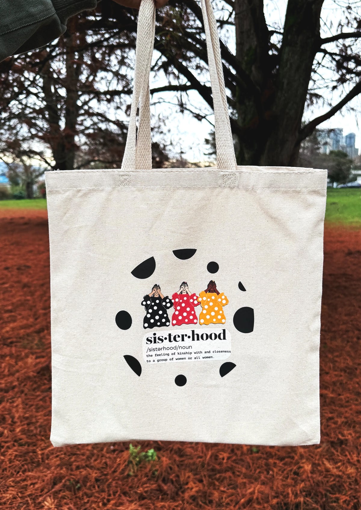 Sisterhood line art canvas tote bag carried outdoors with green grass and mountains in background