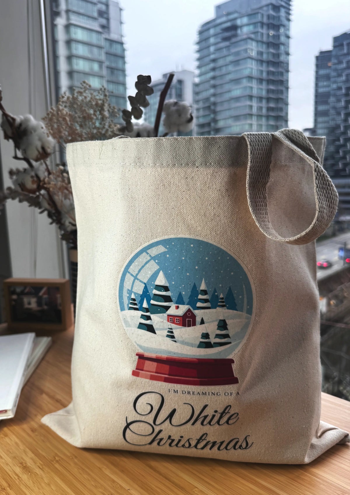 Snow globe winter scene canvas tote bag styled on a wooden table with city skyline in the background