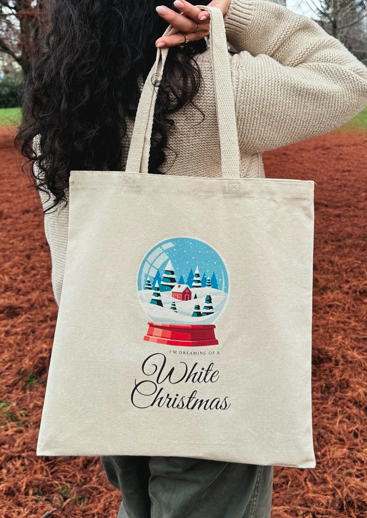 Snow globe winter scene canvas tote bag worn over the shoulder from the back in an outdoor setting