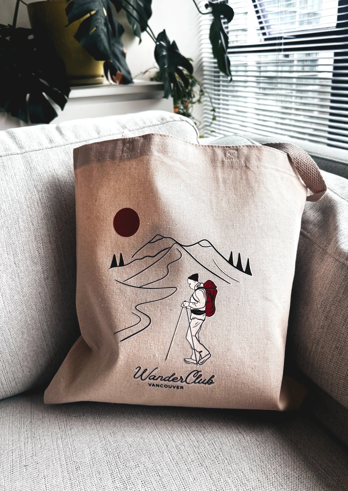 Beige tote bag with mountain and backpack design on a couch