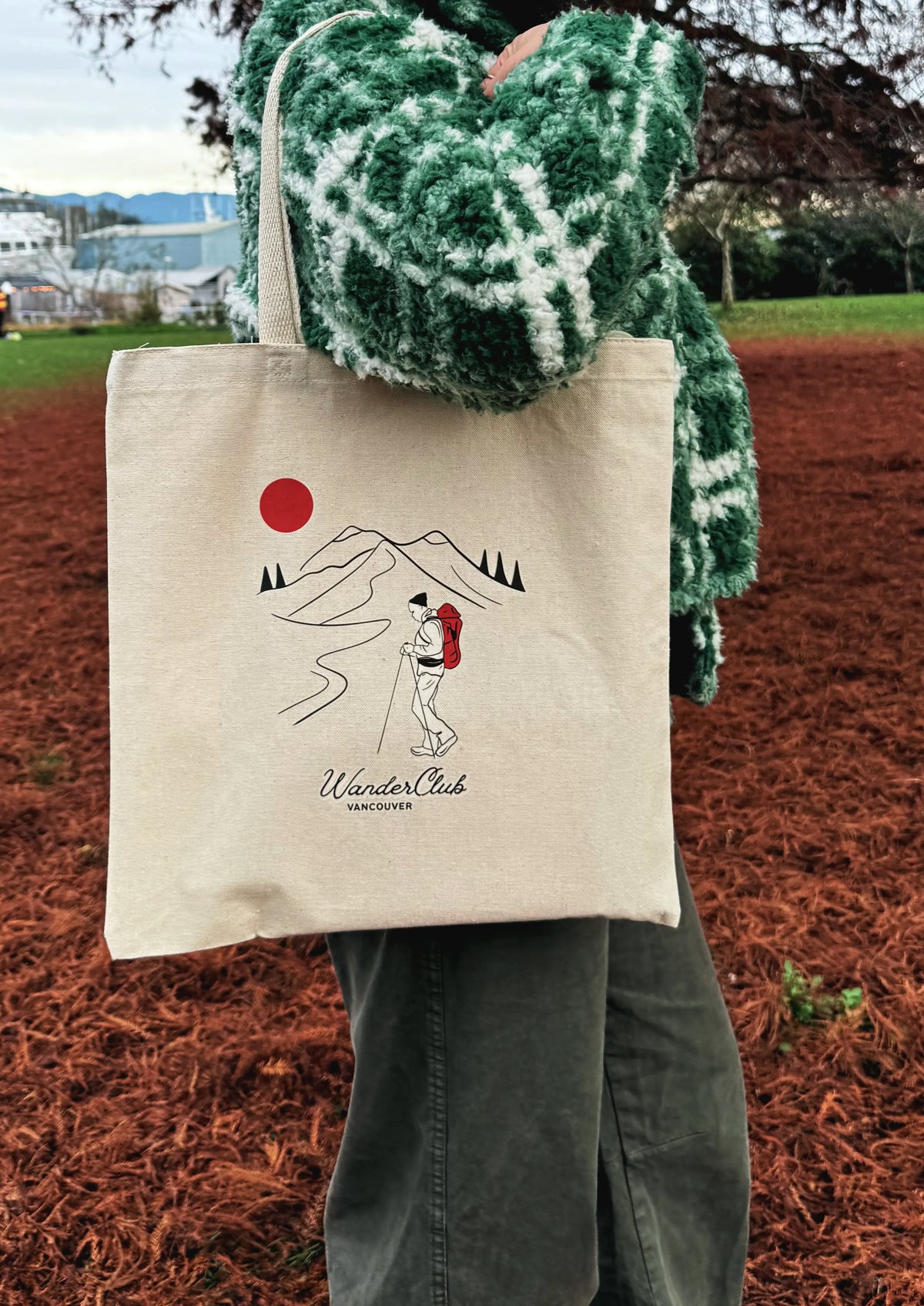 Person holding a tote bag with a mountain and sun design outdoors