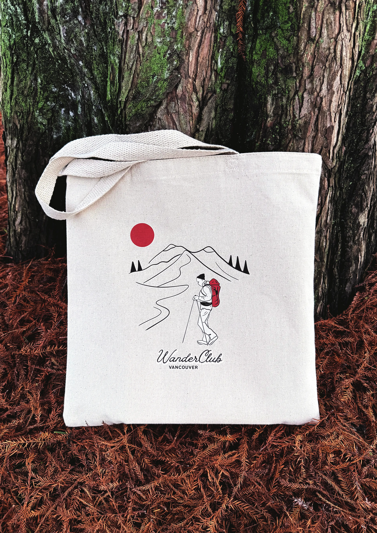 White tote bag with mountain and sun design on a forest floor