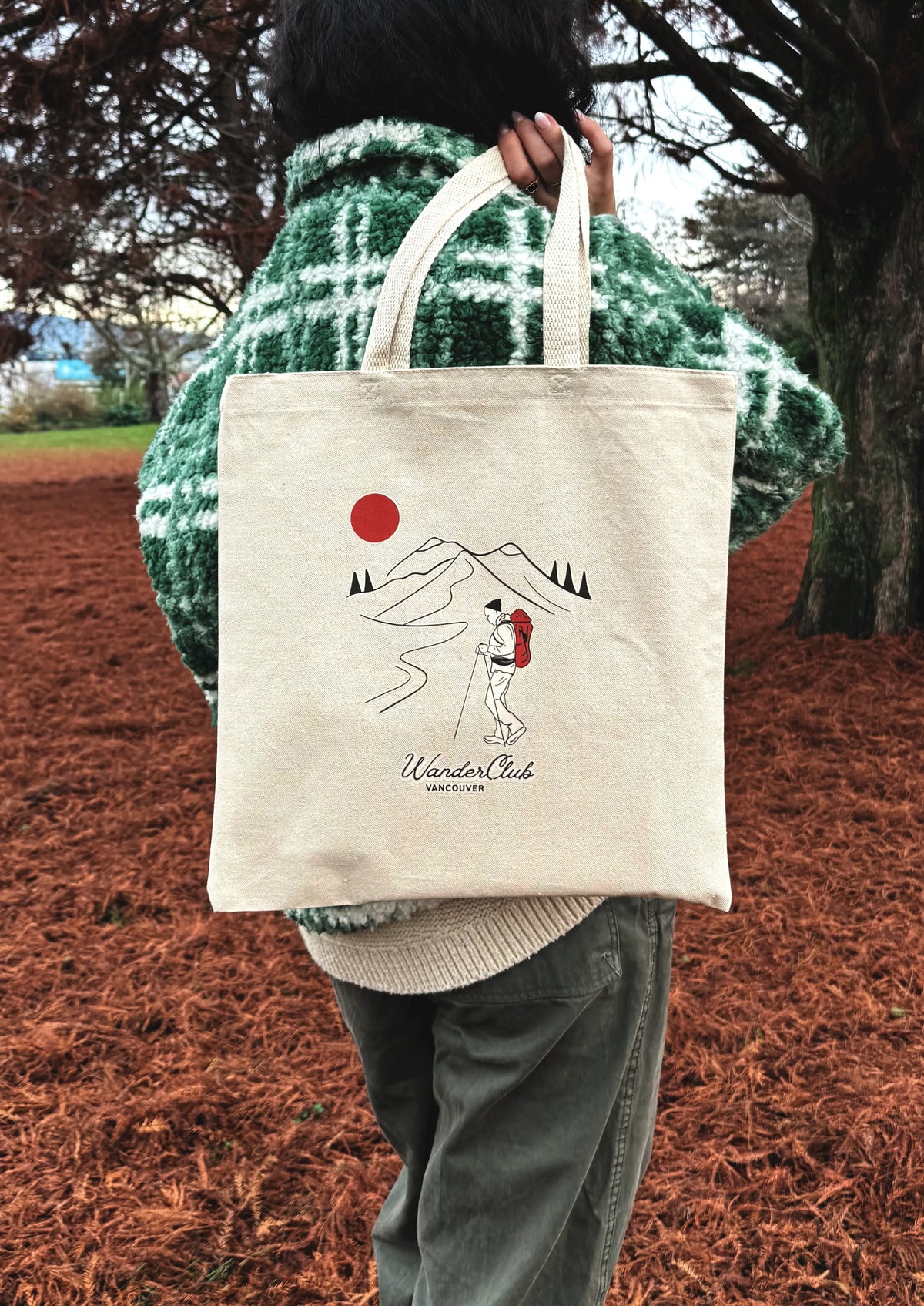 Person holding a tote bag with a design of a couple under a red sun and mountains, standing outdoors.
