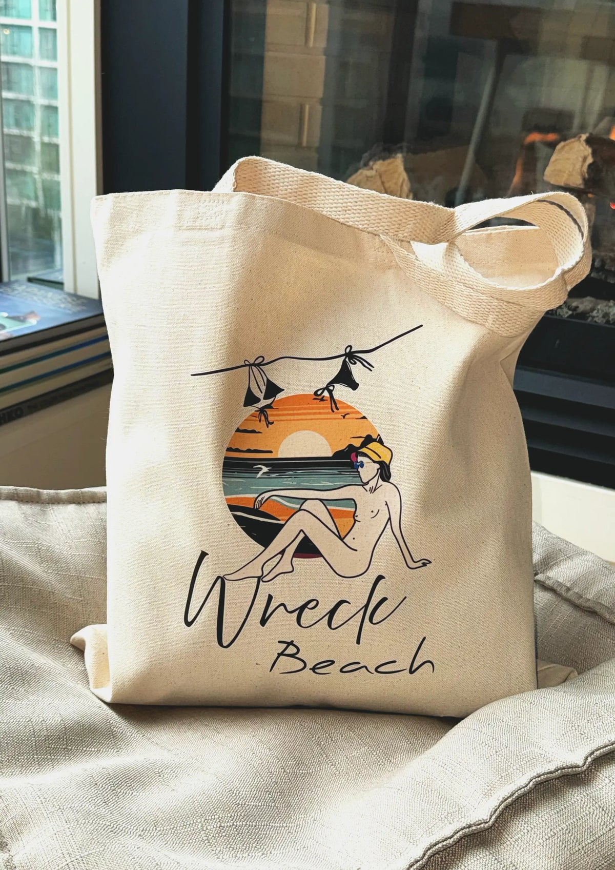 Wreck Beach canvas tote bag resting indoors near a fireplace showcasing sunset beach artwork