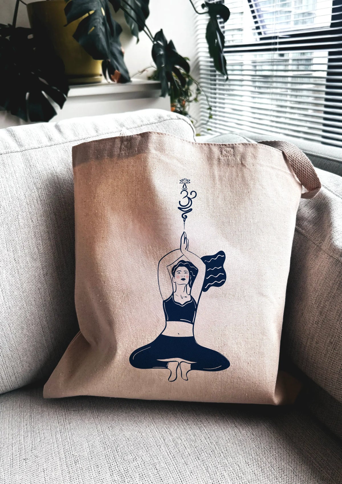 Yoga Flow canvas tote bag with blue line art yoga illustration, displayed indoors on a couch near a window.