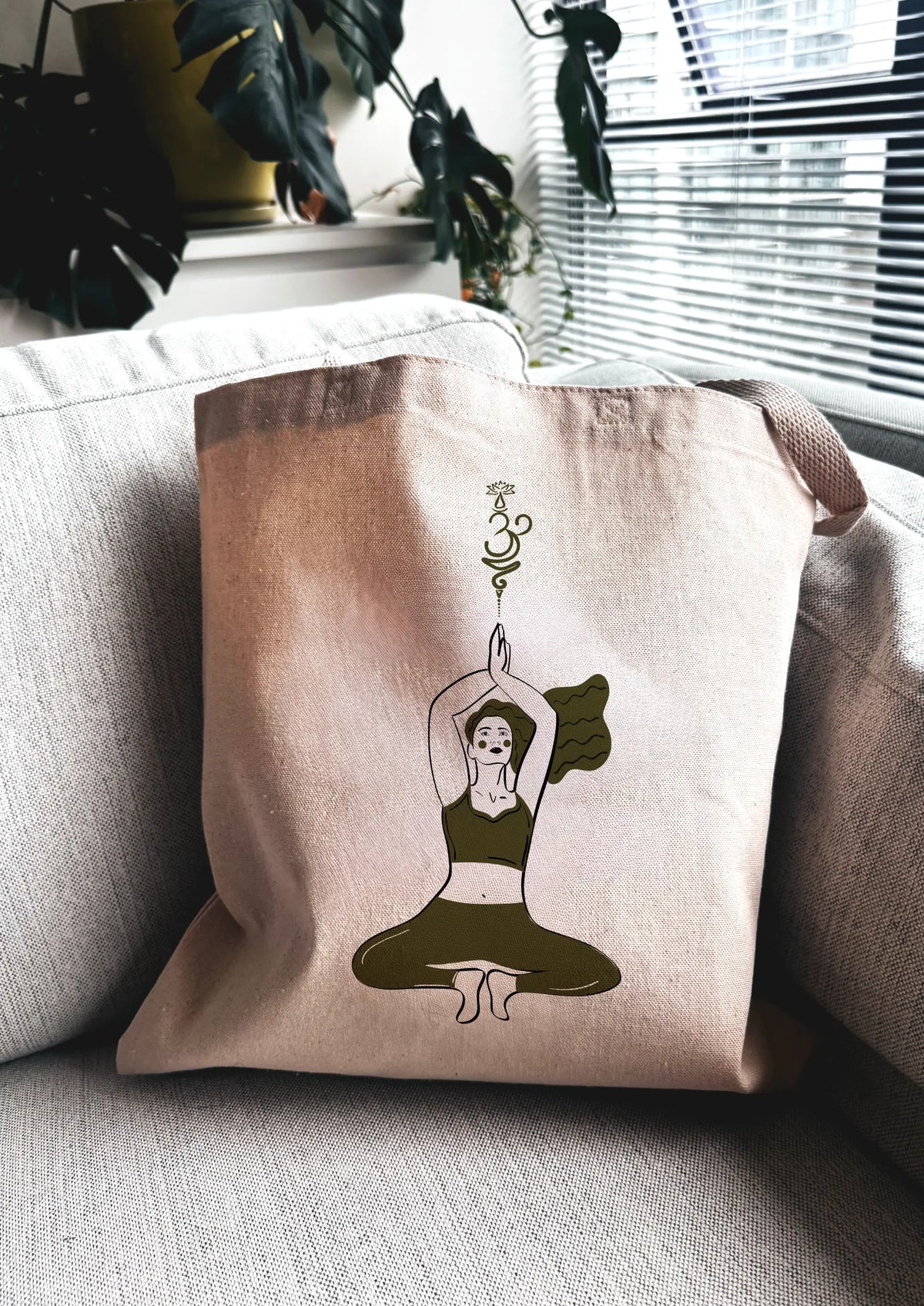 Yoga Flow canvas tote bag with green line art yoga illustration, photographed indoors on a couch.