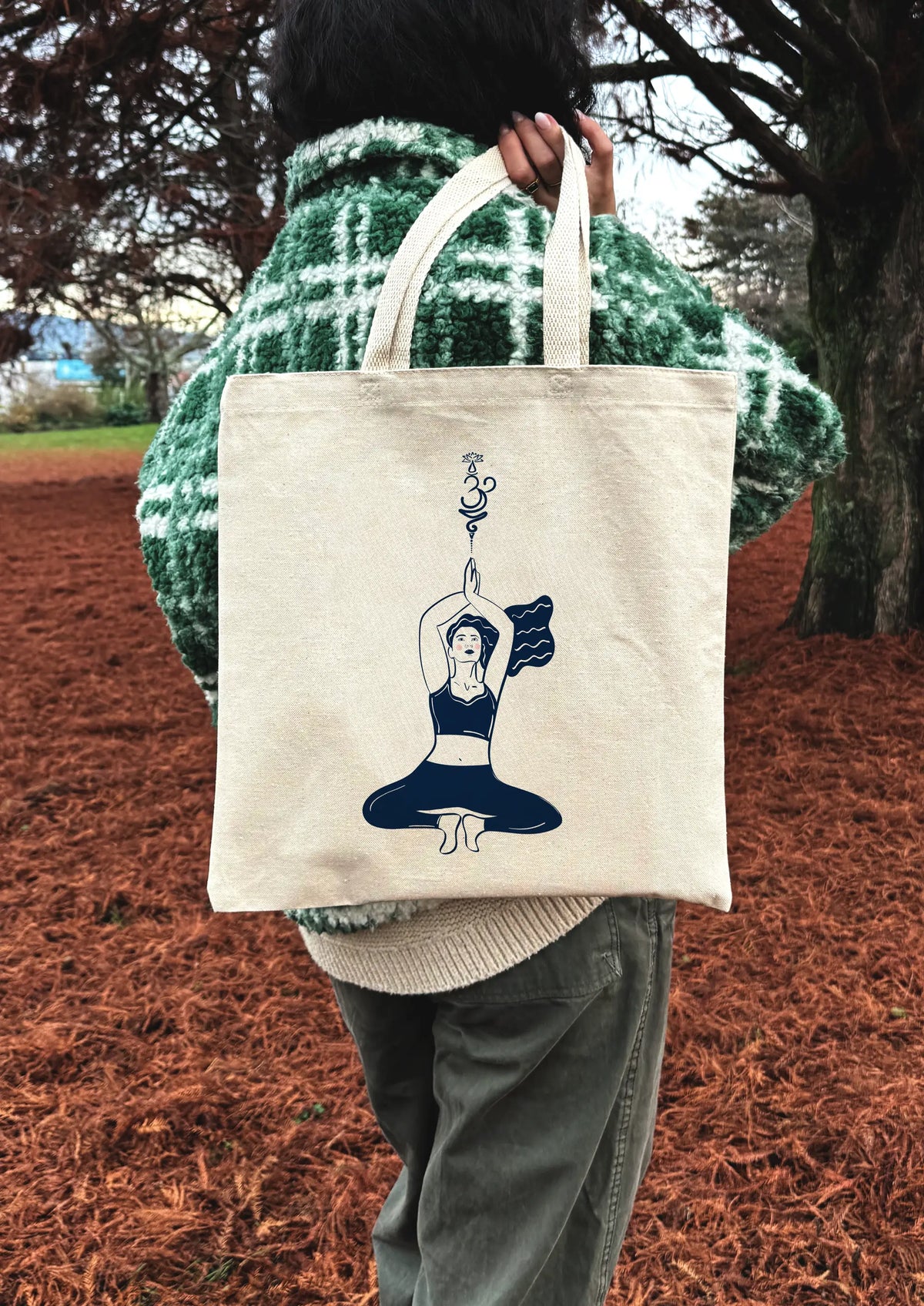 Yoga Flow canvas tote bag worn over the shoulder, showing line art yoga illustration, photographed outdoors.
