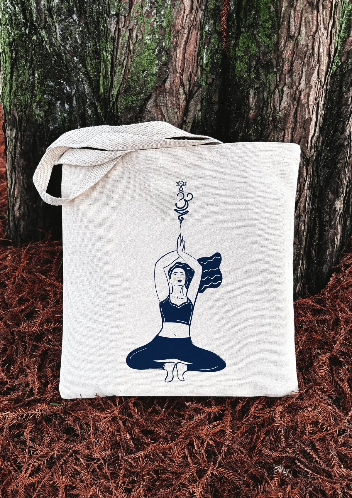 Yoga Flow canvas tote bag with seated yoga illustration, placed against a tree trunk outdoors.