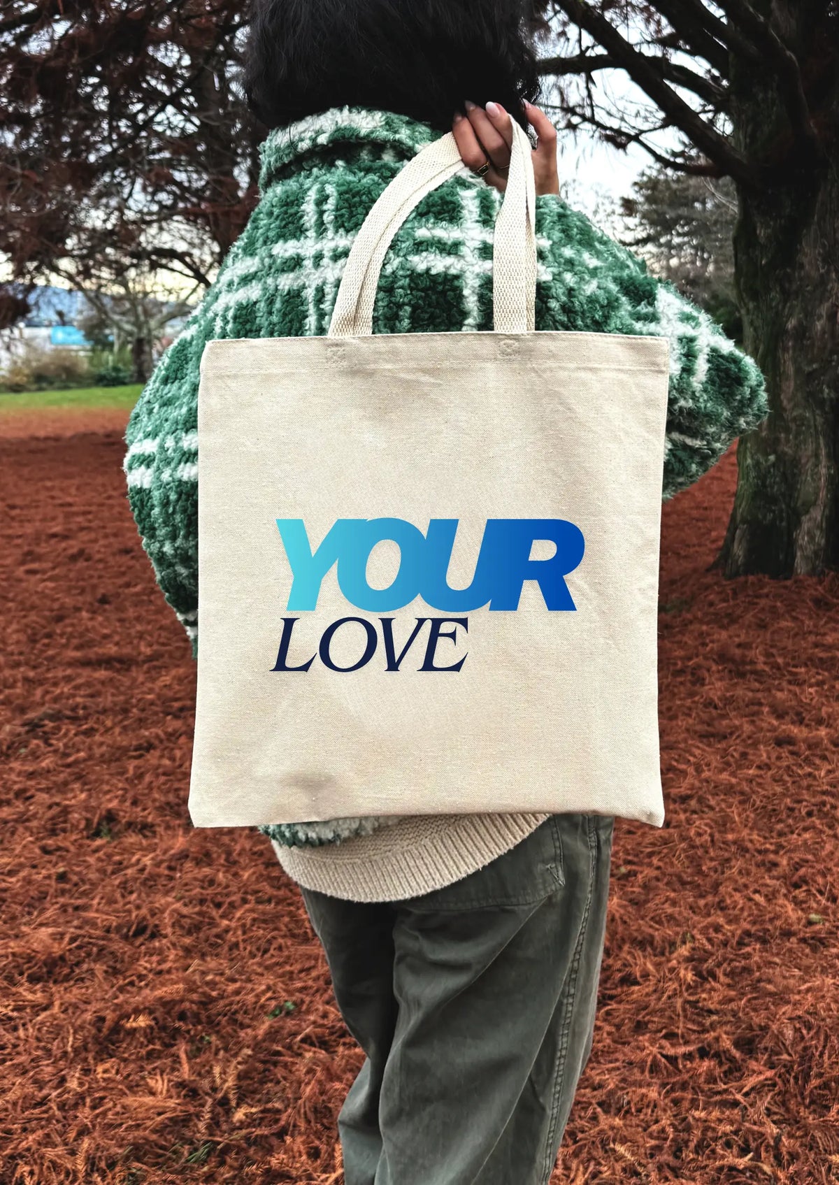 Person holding a tote bag with 'YOUR LOVE' text outdoors