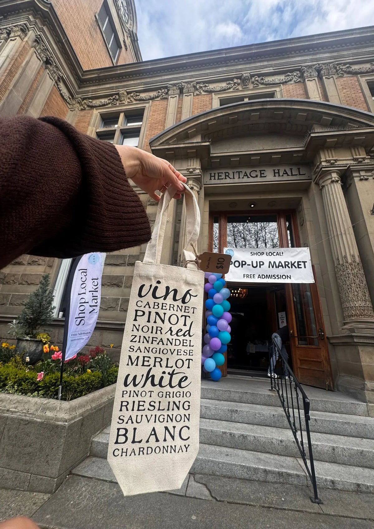 Person holding a tote bag with wine list text in front of Heritage Hall.